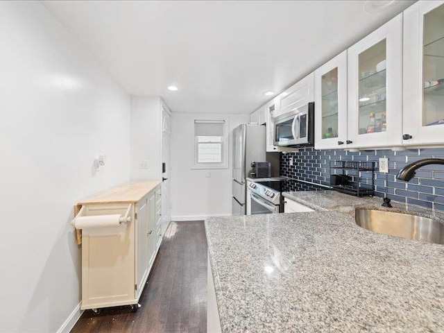 kitchen featuring light stone counters, decorative backsplash, appliances with stainless steel finishes, white cabinets, and a sink