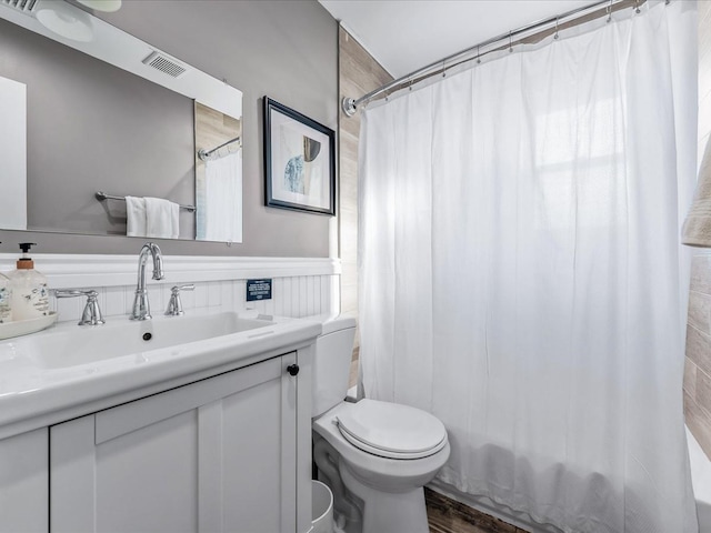 full bathroom featuring visible vents, toilet, shower / bath combo with shower curtain, wainscoting, and vanity