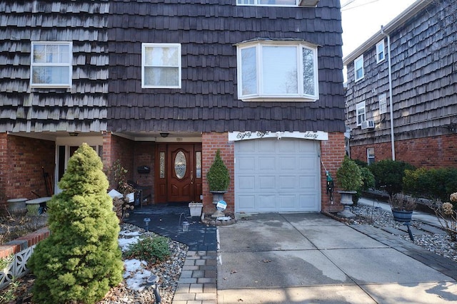 view of front facade with driveway, brick siding, mansard roof, and an attached garage