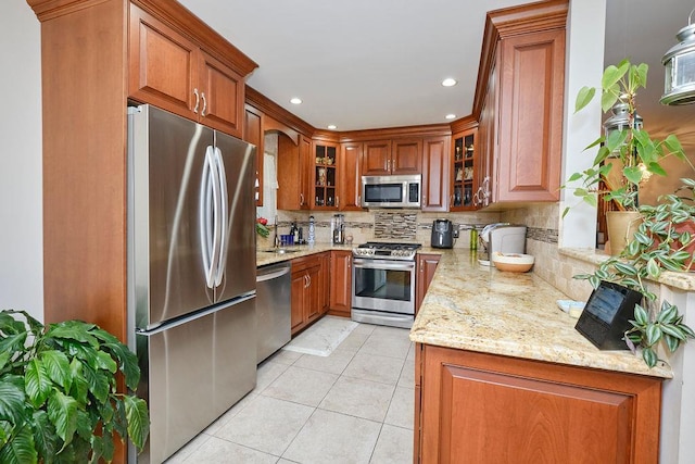 kitchen featuring light stone counters, light tile patterned floors, stainless steel appliances, backsplash, and brown cabinetry