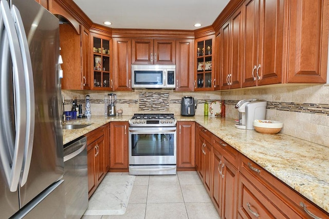 kitchen with brown cabinets, light stone countertops, glass insert cabinets, and stainless steel appliances