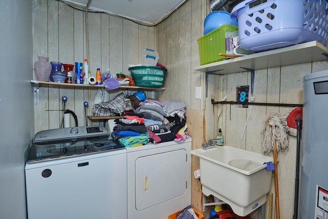 washroom featuring water heater, washing machine and dryer, a sink, wooden walls, and laundry area