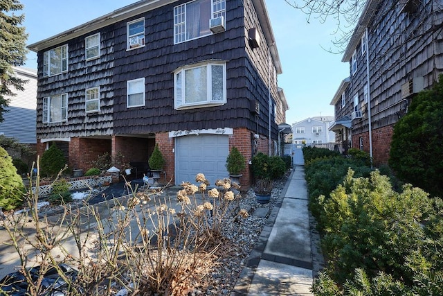 view of side of property featuring an attached garage, driveway, cooling unit, and brick siding