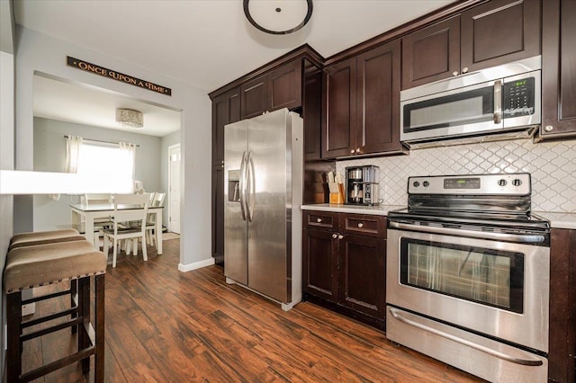 kitchen featuring dark brown cabinetry, appliances with stainless steel finishes, decorative backsplash, and dark wood-type flooring