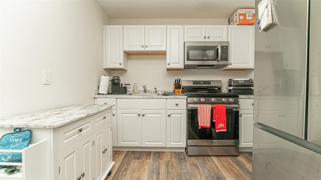 kitchen featuring stainless steel appliances, white cabinetry, a sink, and wood finished floors