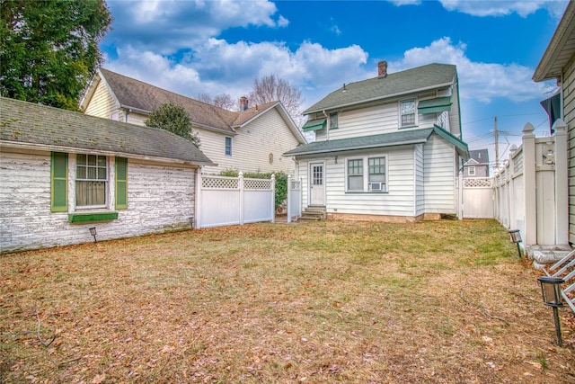 back of house featuring entry steps, a lawn, a chimney, and a fenced backyard