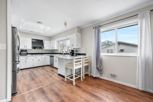 kitchen featuring stainless steel appliances, range hood, visible vents, and tasteful backsplash