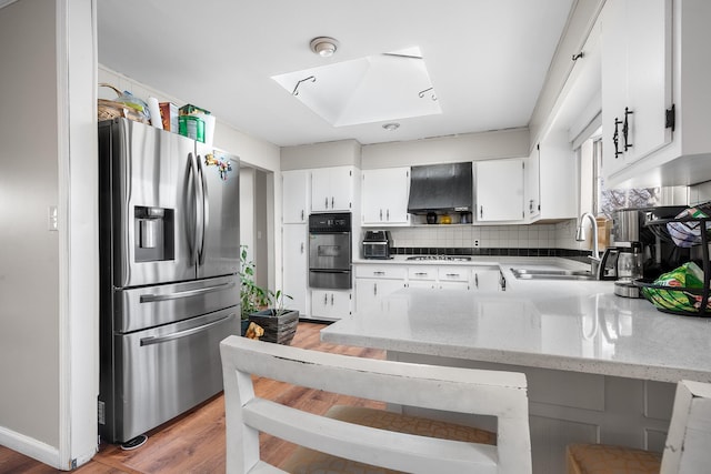 kitchen featuring stainless steel appliances, a skylight, a sink, range hood, and a warming drawer