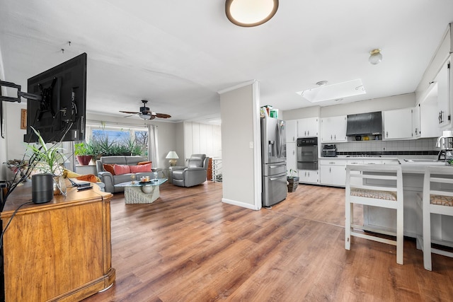 kitchen featuring range hood, light wood-style flooring, decorative backsplash, white cabinets, and stainless steel fridge