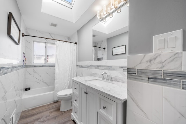 full bathroom with toilet, a skylight, wood finished floors, tile walls, and shower / bath combo