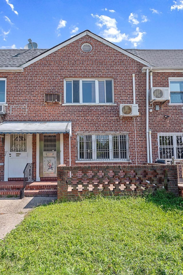 view of front of home with an AC wall unit, brick siding, a front yard, and a wall mounted air conditioner