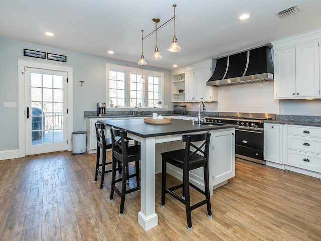 kitchen featuring open shelves, a sink, double oven range, wall chimney exhaust hood, and dark countertops