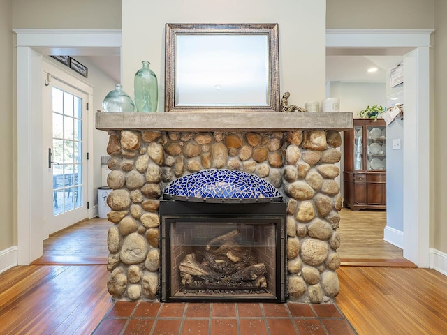 details featuring a stone fireplace, baseboards, and wood finished floors