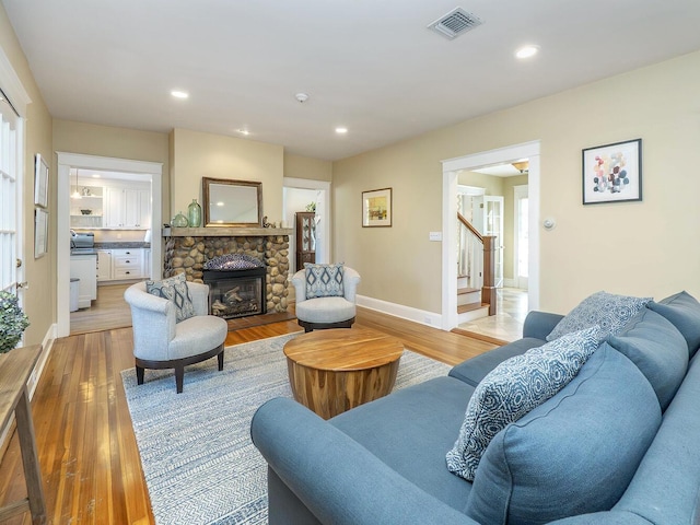 living area with a stone fireplace, recessed lighting, visible vents, stairs, and light wood-type flooring