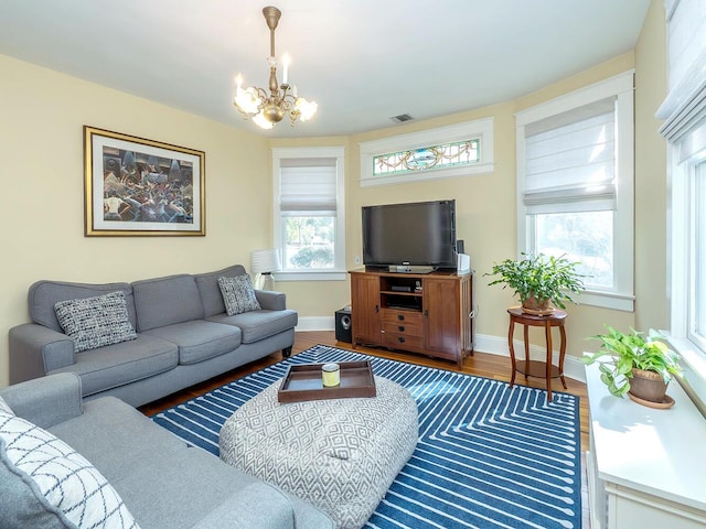 living area with a chandelier, wood finished floors, visible vents, and baseboards