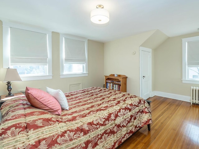 bedroom with radiator, multiple windows, hardwood / wood-style flooring, and baseboards