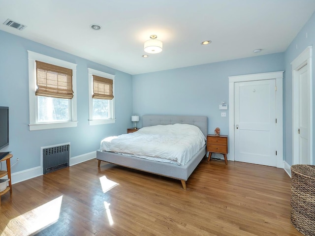 bedroom with radiator heating unit, visible vents, baseboards, and wood finished floors