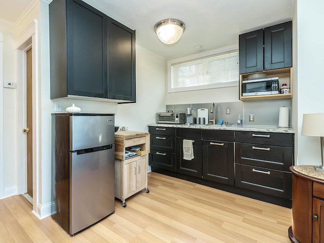 kitchen featuring appliances with stainless steel finishes, light wood-type flooring, a sink, and crown molding