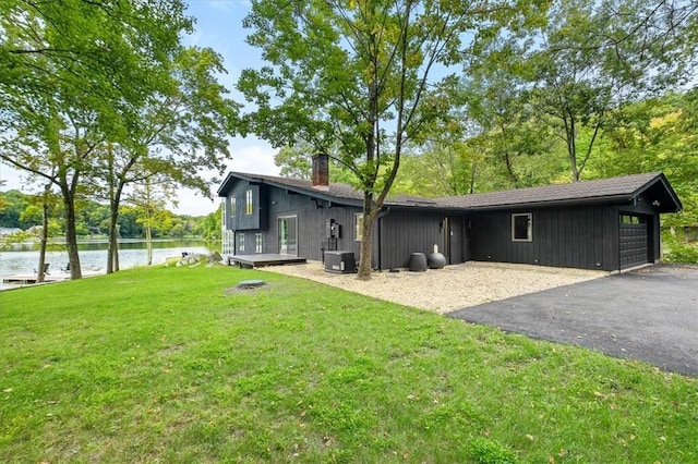 rear view of house featuring aphalt driveway, cooling unit, a garage, a yard, and a chimney