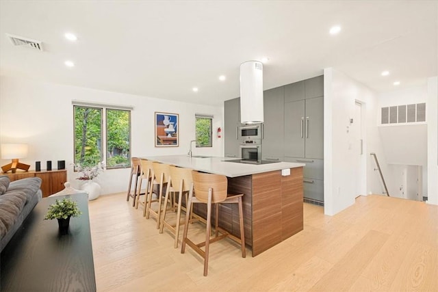 kitchen with light wood-type flooring, a kitchen bar, modern cabinets, and visible vents