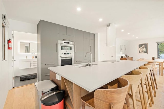 kitchen with double oven, light wood-style floors, gray cabinets, and a sink