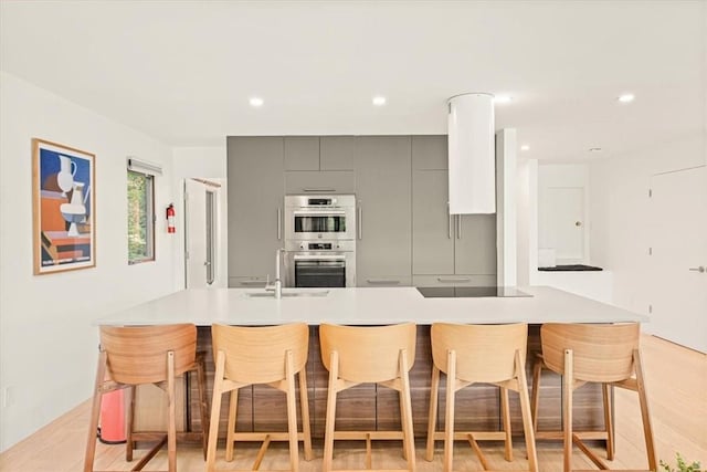 kitchen featuring black electric cooktop, double oven, a kitchen bar, and gray cabinets