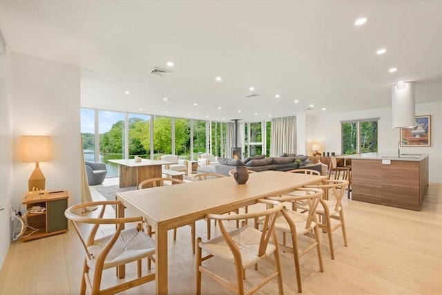 dining room featuring light wood-style flooring, a wall of windows, plenty of natural light, and visible vents