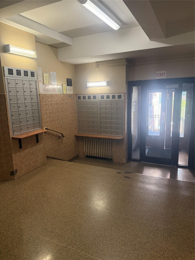 interior space with mail area, radiator heating unit, tile walls, and a wainscoted wall