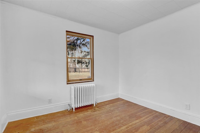 empty room featuring radiator, light wood-style floors, and baseboards