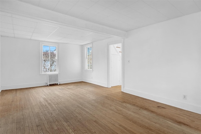 unfurnished room featuring radiator, hardwood / wood-style flooring, and baseboards