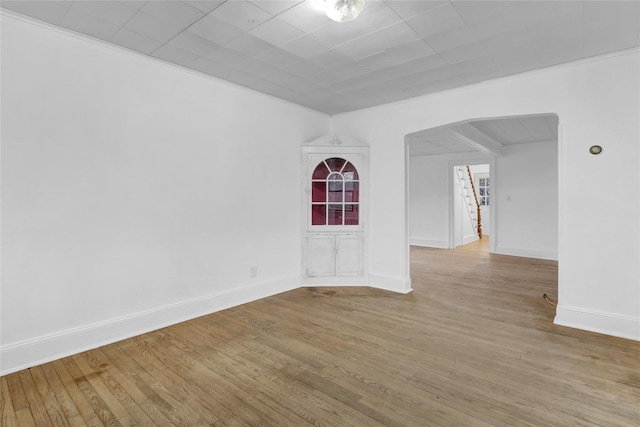 empty room featuring baseboards, arched walkways, and wood finished floors