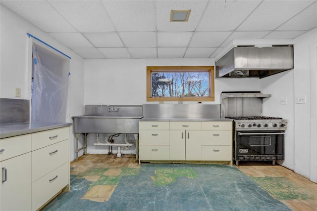 kitchen featuring stainless steel gas stove, a drop ceiling, wall chimney range hood, stainless steel counters, and a sink