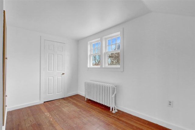 unfurnished bedroom featuring lofted ceiling, radiator heating unit, wood-type flooring, and baseboards