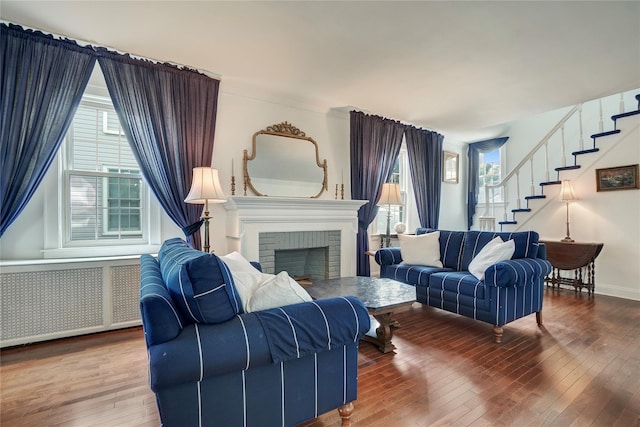 living room featuring a brick fireplace, stairway, radiator heating unit, and hardwood / wood-style flooring