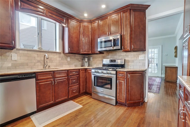 kitchen with tasteful backsplash, light wood-style flooring, appliances with stainless steel finishes, ornamental molding, and a sink