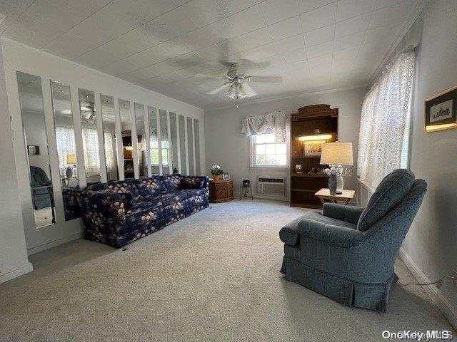 carpeted living room with a wall mounted air conditioner, a ceiling fan, and baseboards