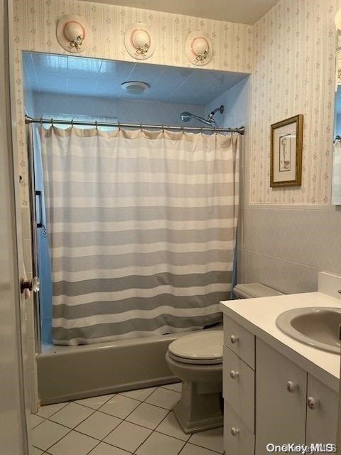 bathroom with wainscoting, tile patterned flooring, shower / bath combo with shower curtain, and wallpapered walls