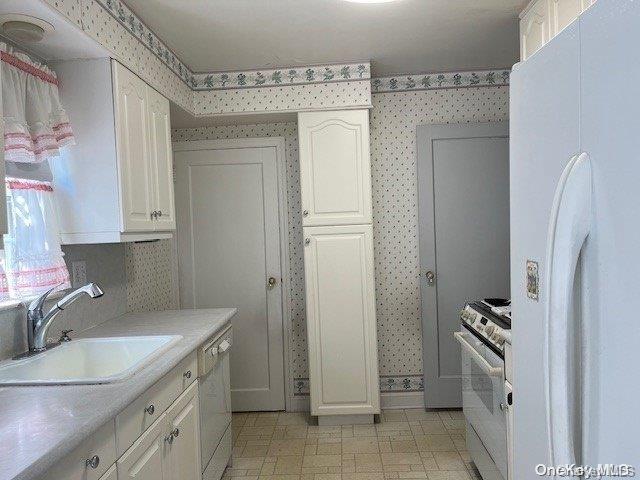 kitchen featuring light countertops, white cabinetry, a sink, white appliances, and wallpapered walls