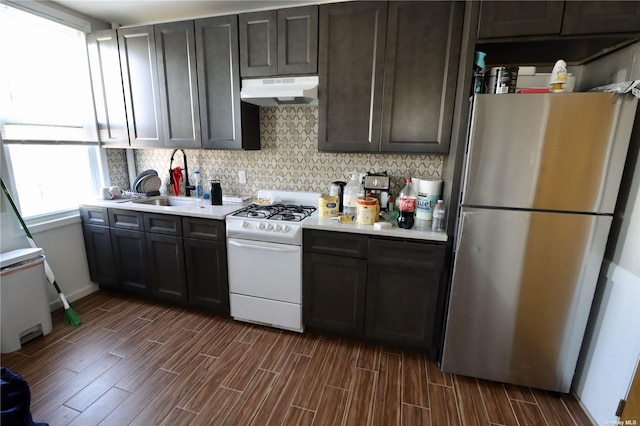 kitchen with white gas stove, under cabinet range hood, light countertops, freestanding refrigerator, and wood tiled floor