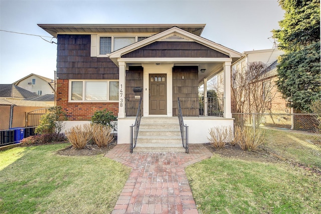 view of front of house with covered porch, brick siding, a front yard, and fence