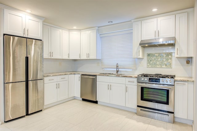 kitchen with light stone counters, appliances with stainless steel finishes, white cabinets, a sink, and under cabinet range hood