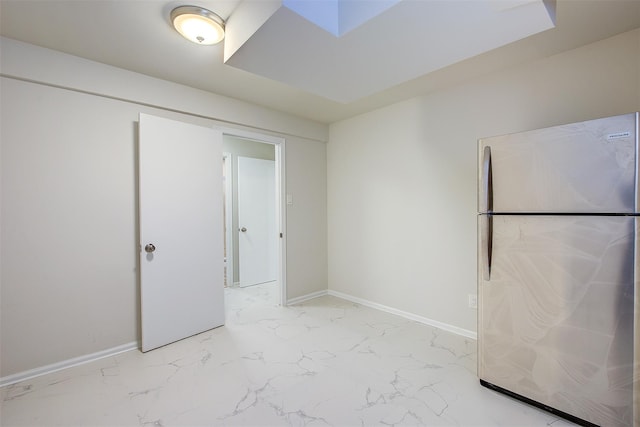 unfurnished bedroom featuring marble finish floor, baseboards, and freestanding refrigerator