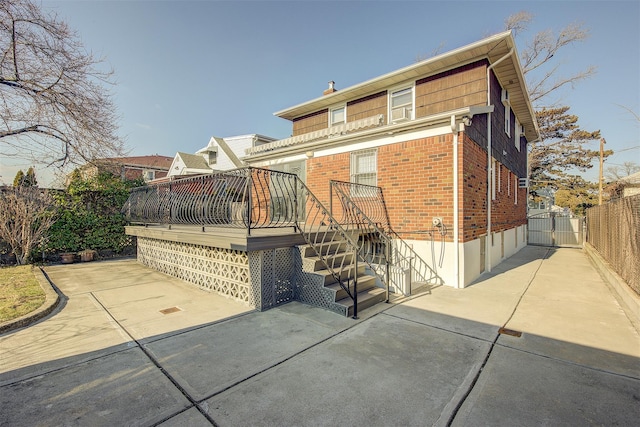 view of front of house with a deck, brick siding, fence, a gate, and a patio area