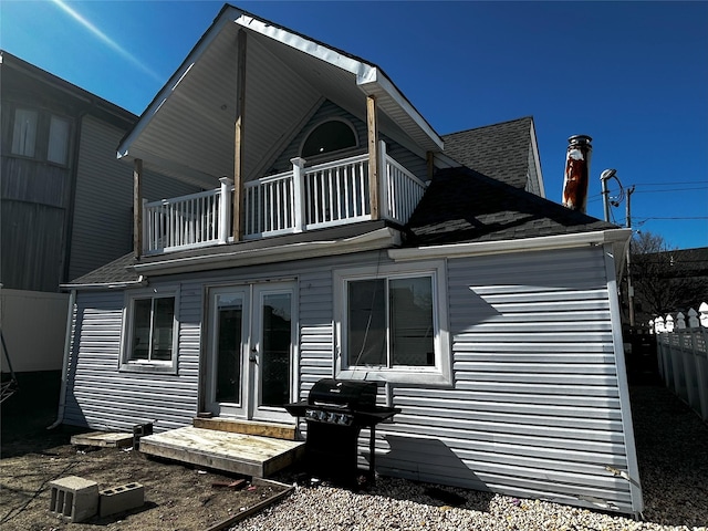 back of property featuring french doors, roof with shingles, fence, and a balcony