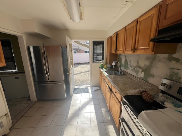 kitchen with light tile patterned floors, stainless steel appliances, brown cabinetry, a sink, and under cabinet range hood