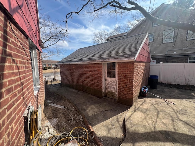 view of property exterior with a shingled roof, brick siding, fence, and a patio