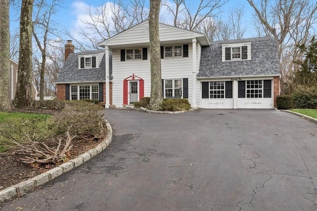 view of front facade with aphalt driveway, a garage, brick siding, roof with shingles, and a chimney