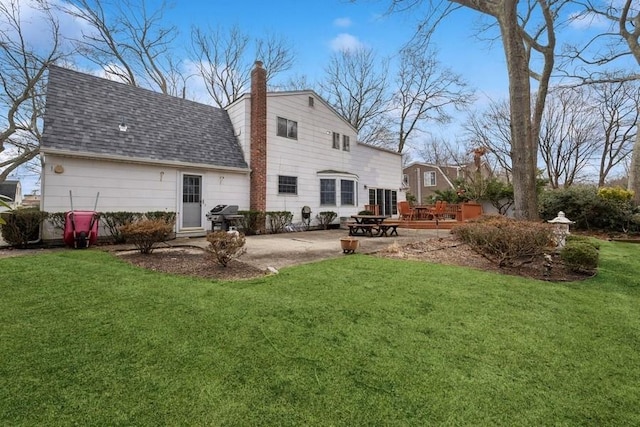 back of property with a patio area, roof with shingles, a chimney, and a yard