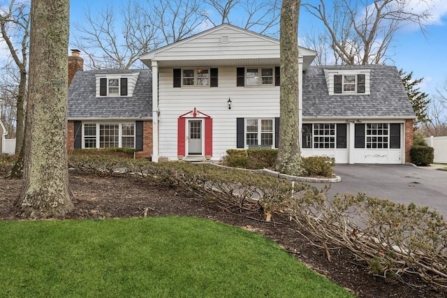 view of front of home with aphalt driveway, a garage, brick siding, a shingled roof, and a chimney