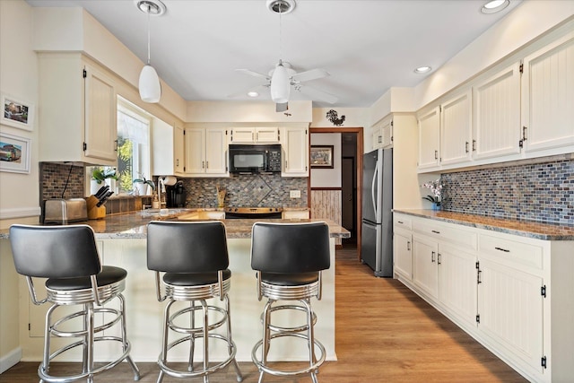 kitchen featuring light wood-style floors, freestanding refrigerator, light stone countertops, black microwave, and a peninsula